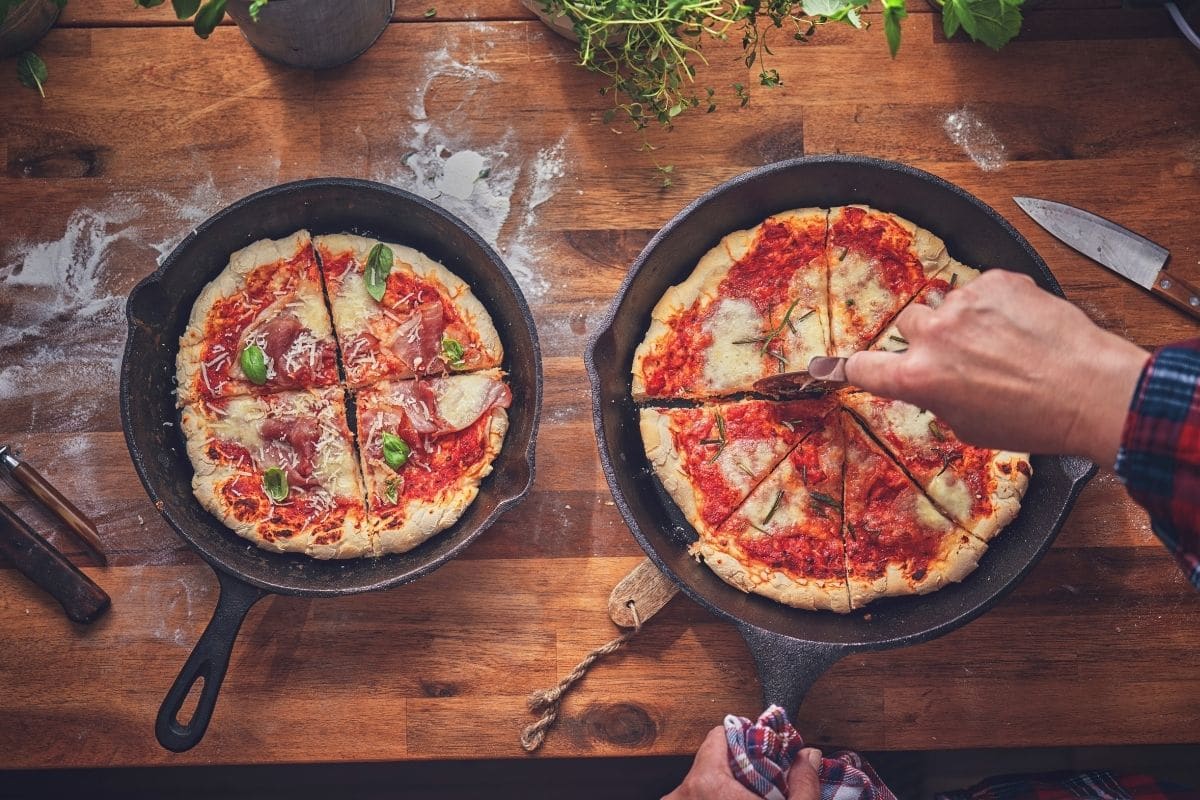 overhead shot of man cutting pizza in a cast iron skillet