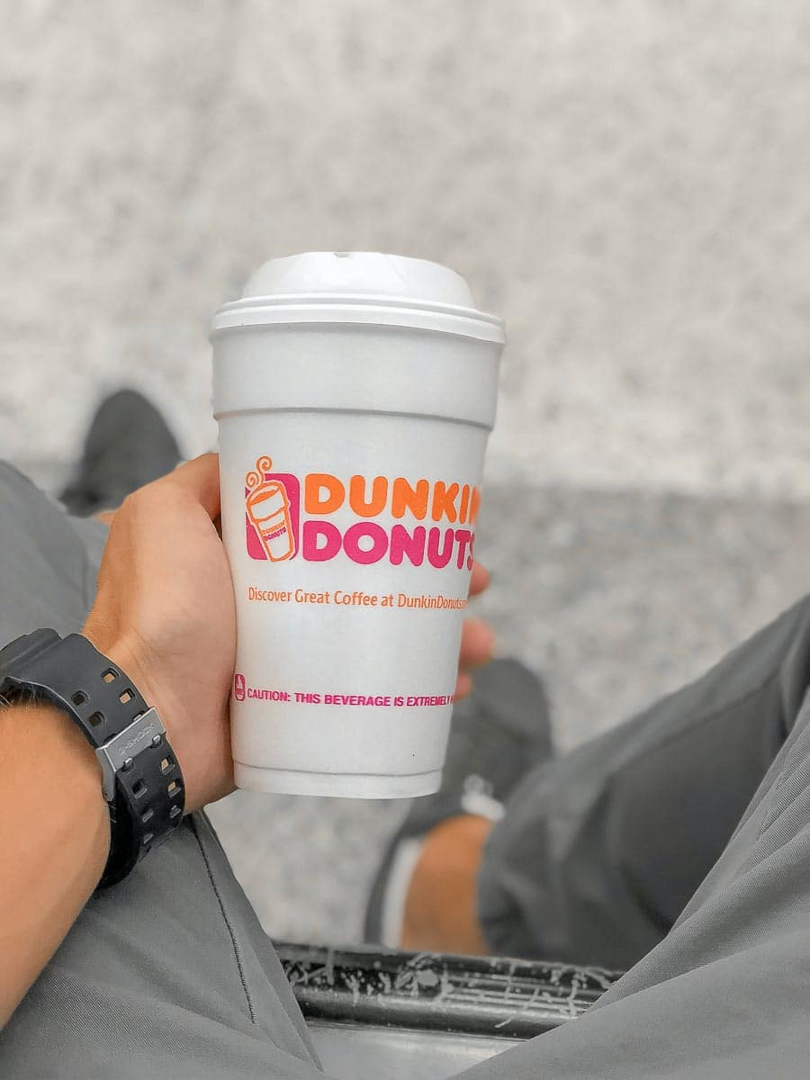 Man's hand holding a Dunkin' Donuts cup between legs.