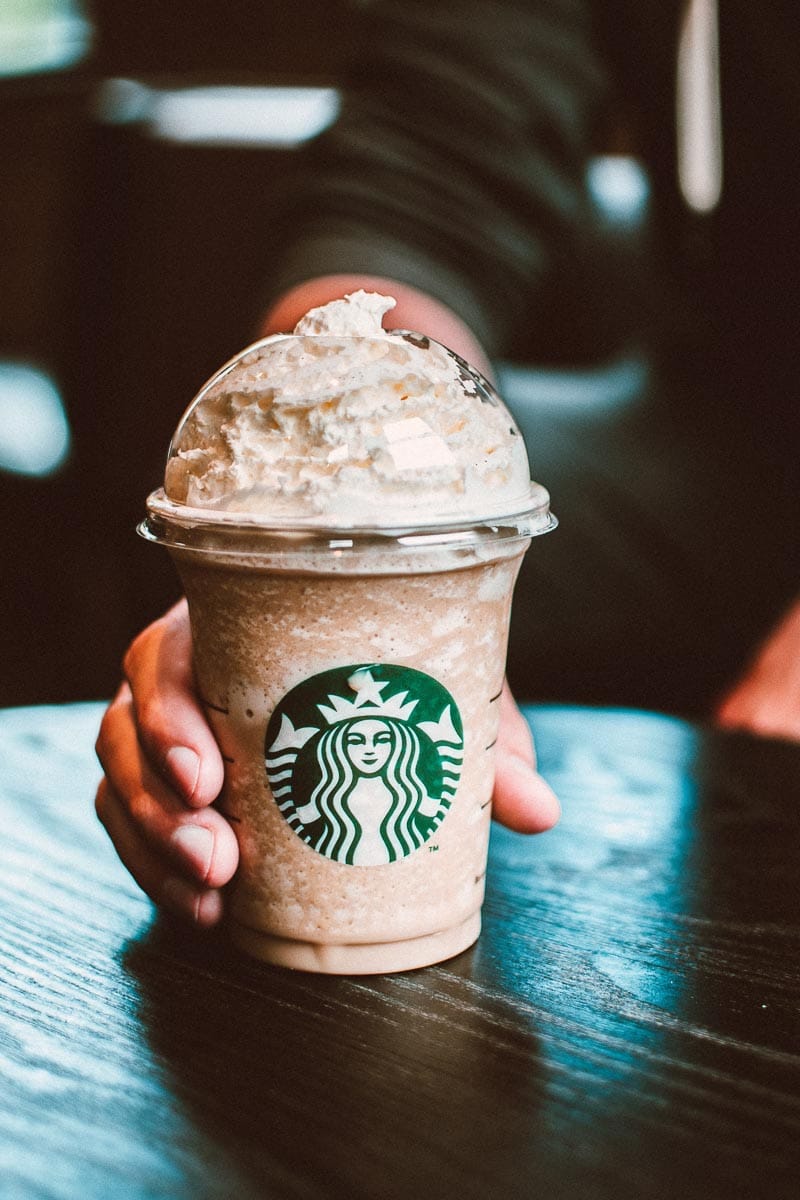 Starbucks blended drink on dark counter held by man's hand.