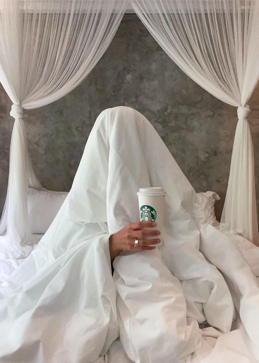 Person hiding under white cover holding Starbucks cup.