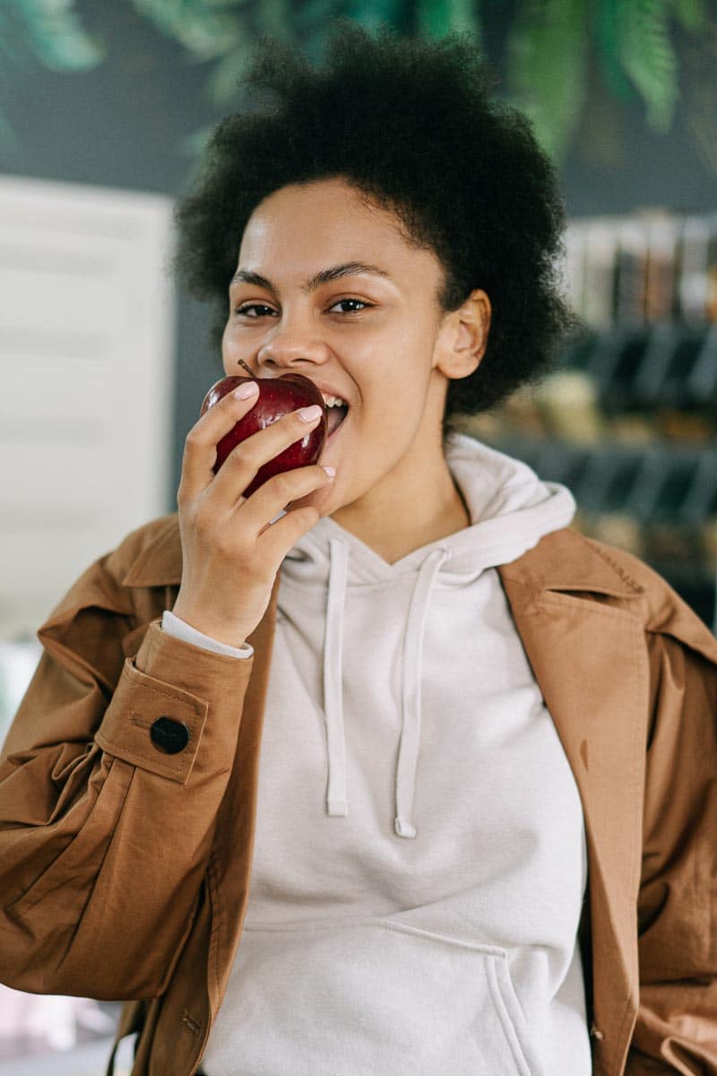 young woman of color eating a red apple, wearing a white top