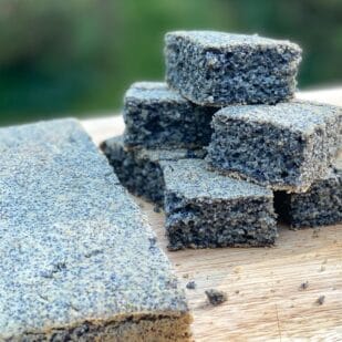Low FODMAP Blue Cornbread, slab on the left, squares stacked on the right, on a wooden board, outdoors