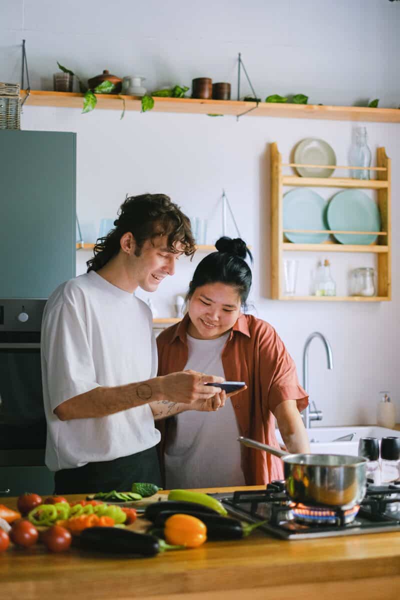 young man and woman checking smartphone while cooking in kitchen