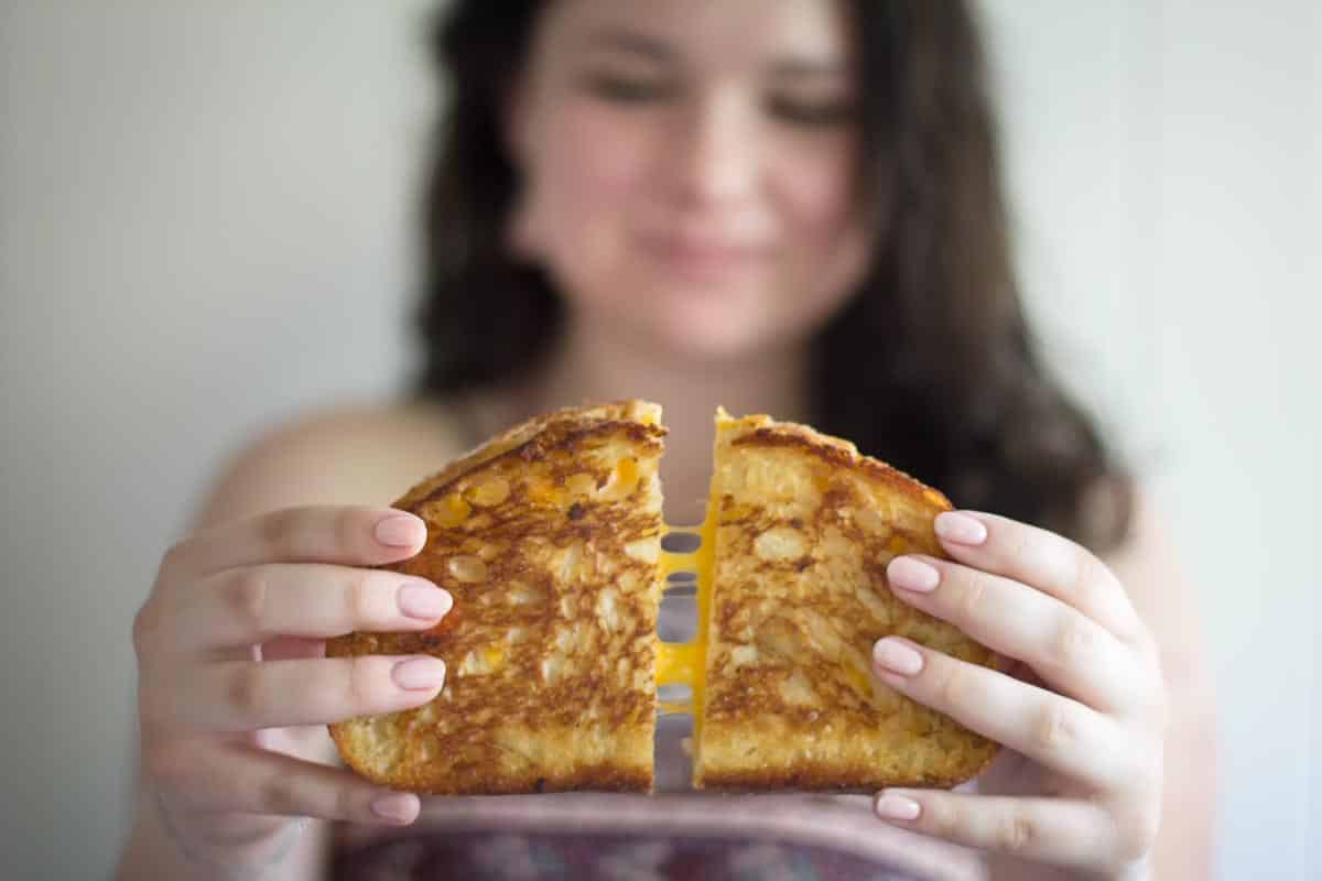 young woman pulling apart grilled cheese sandwich