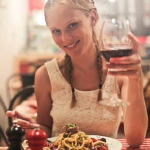 Woman eating spaghetti and drinking wine