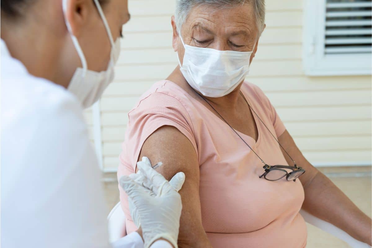 An older woman wearing a face mask receiving a vaccine from a male nurse