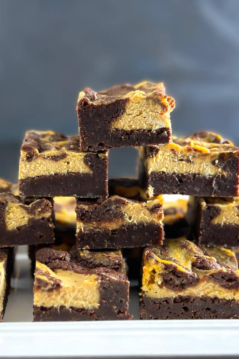 Low FODMAP Pumpkin Cheesecake Brownies stacked on a white plate, dark background, vertical image closeup