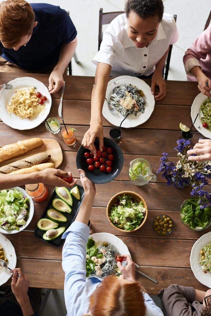 people enjoying a pasta meal around a wooden table