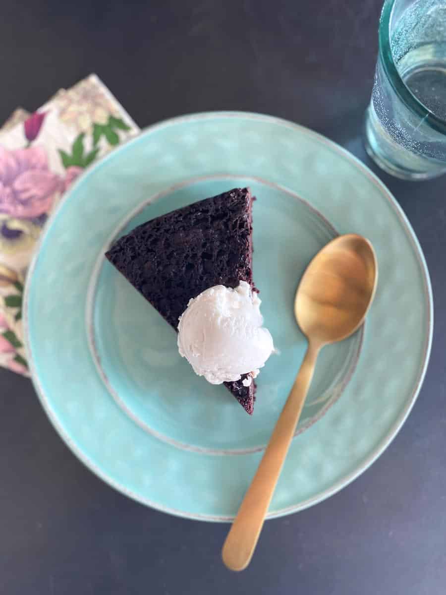 vertical image of wedge of Gluten free Low FODMAP Maple Mocha Cake on aqua plate with vanilla ice cream melting on top with gold spoon alongside