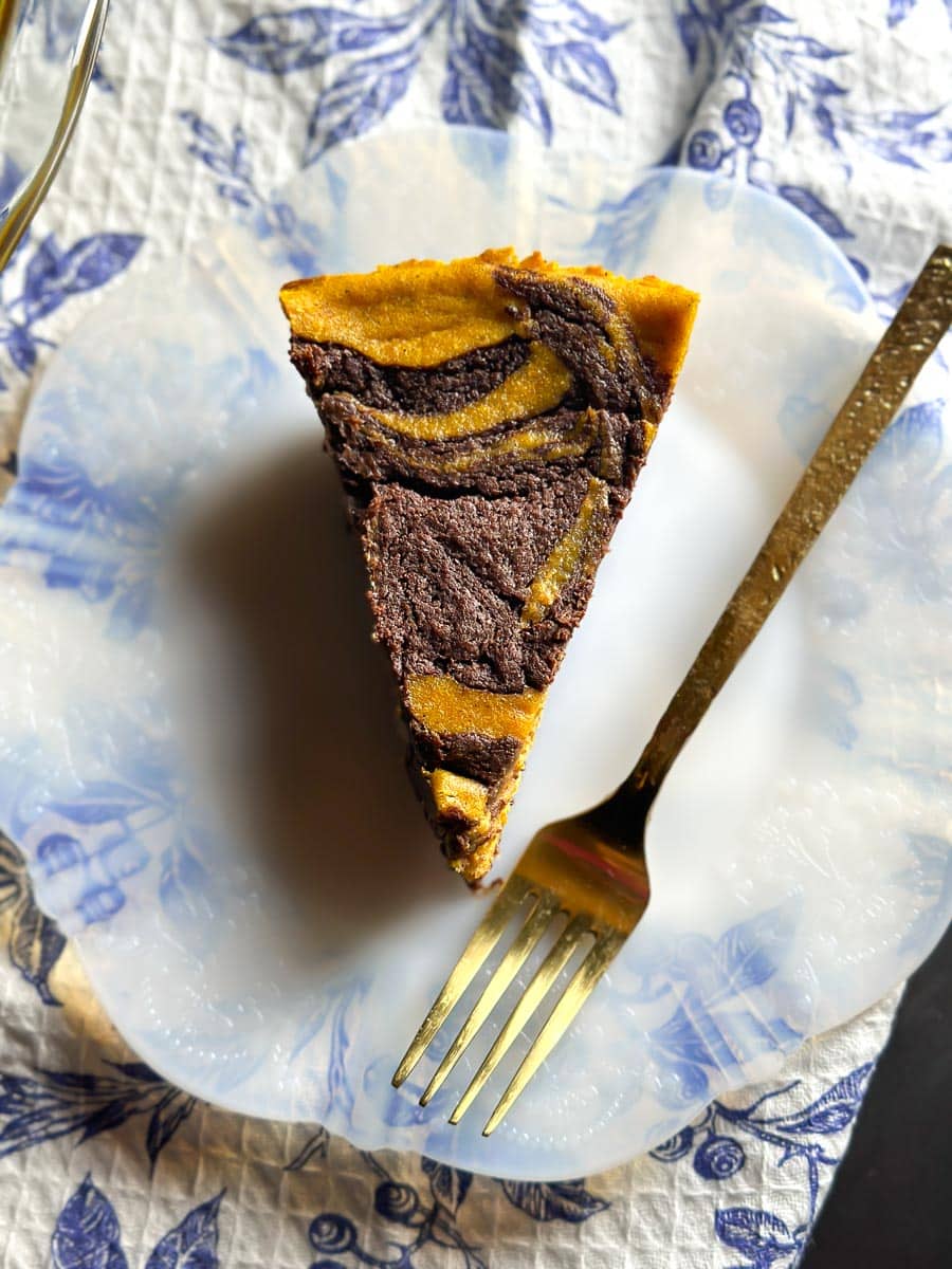 wedge of Low FODMAP Pumpkin Swirl Brownie Pie on depression glass fluted plate; gold fork; blue and white cloth in background