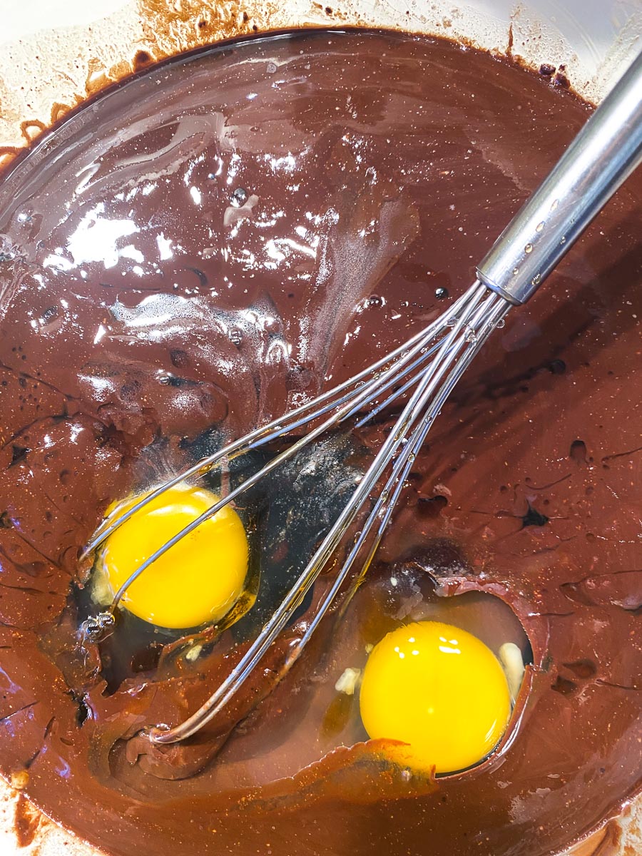 whisking melted chocolate and butter together with eggs in glass bowl