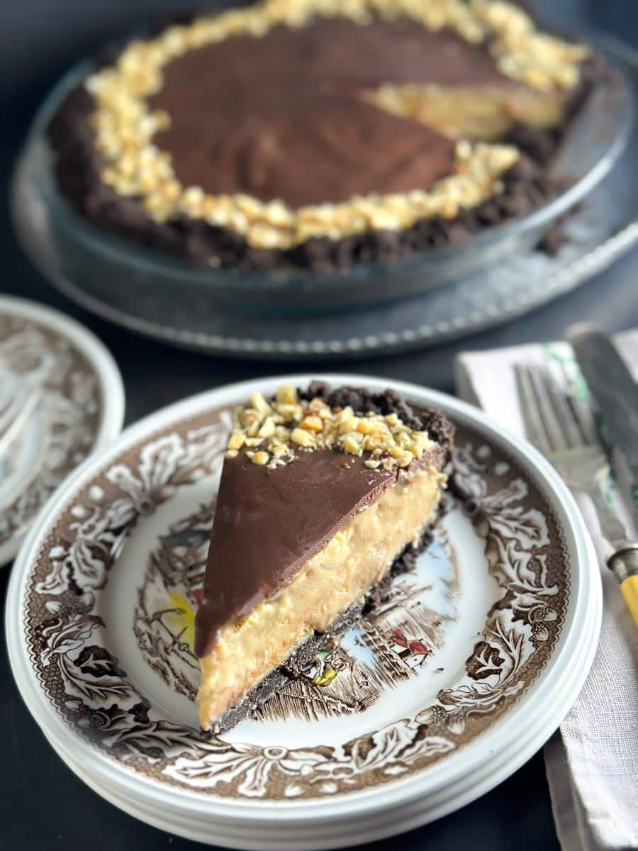 Low FODMAP Chocolate Peanut Butter Pie, dark background; antique plates, silverware and embroidered napkin; wedge on plate