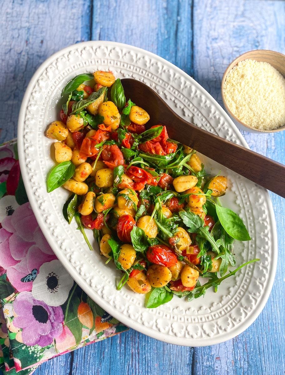 Low FODMAP Roasted Gnocchi With Tomatoes, Basil & Arugula on oval white dish