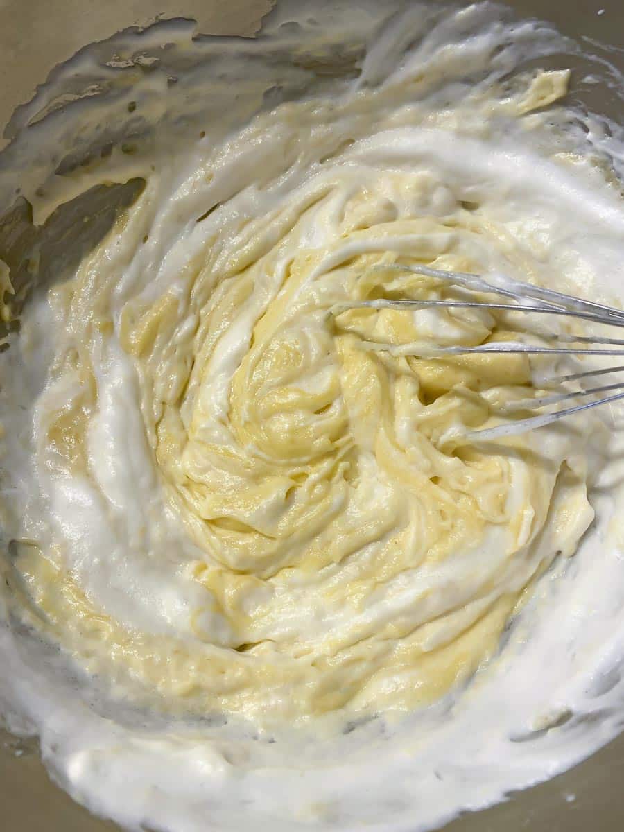 adding whipped egg whites to yellow cake batter in metal bowl