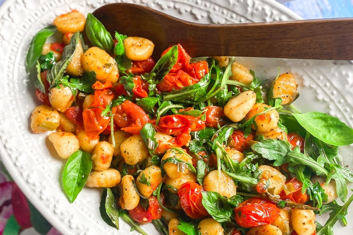 closeup of Low FODMAP Roasted Gnocchi With Tomatoes, Basil & Arugula on oval white dish