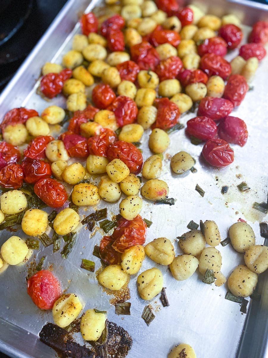 tomatoes and gnocchi tossed together on a sheet pan with oil, scallion greens, salt and pepper, after roasting