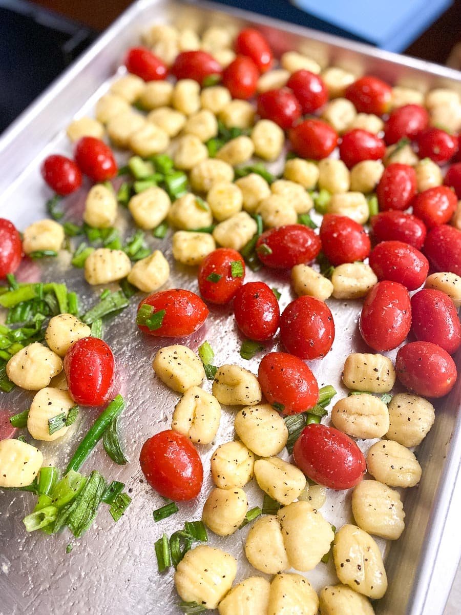 tomatoes and gnocchi tossed together on a sheet pan with oil, scallion greens, salt and pepper