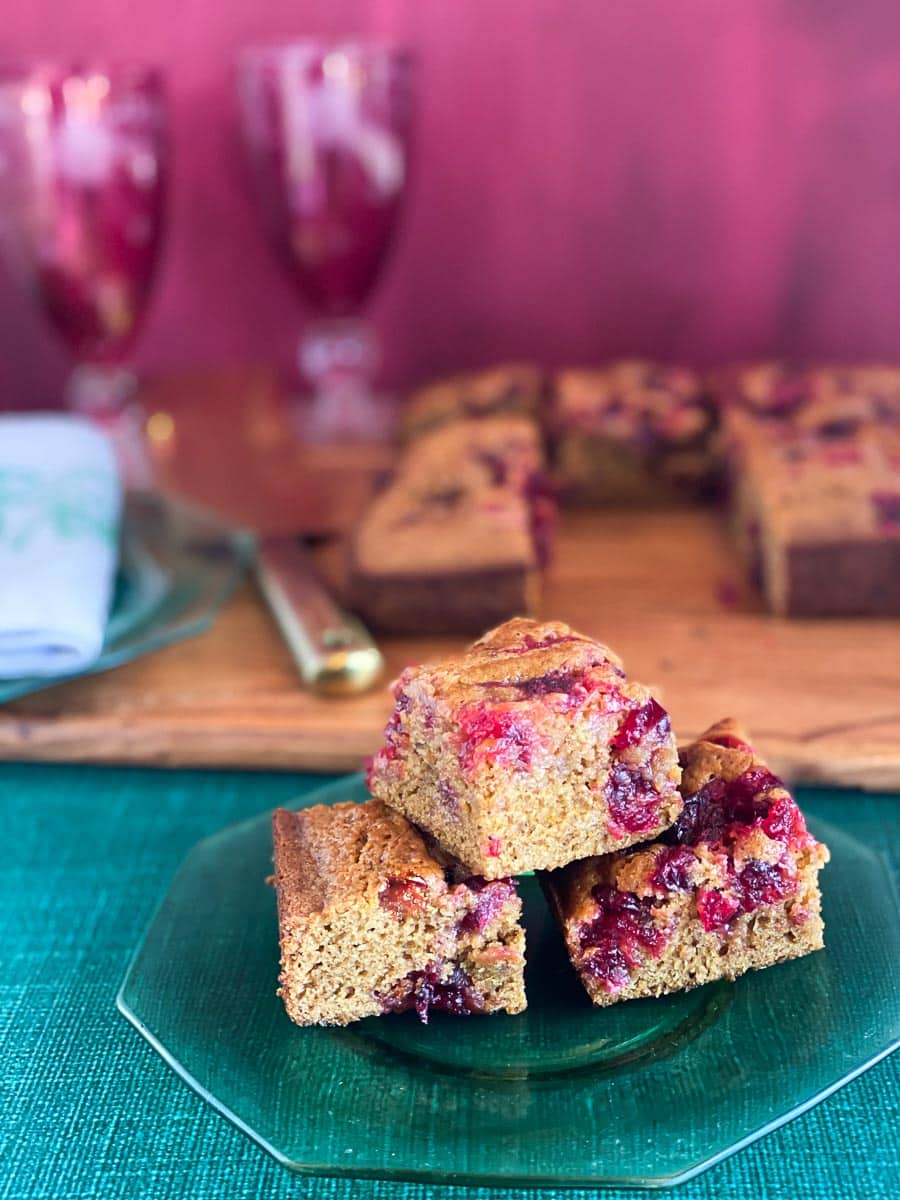 Low FODMAP Sticky Cranberry Gingerbread cut into squares, on wooden board and glass plate