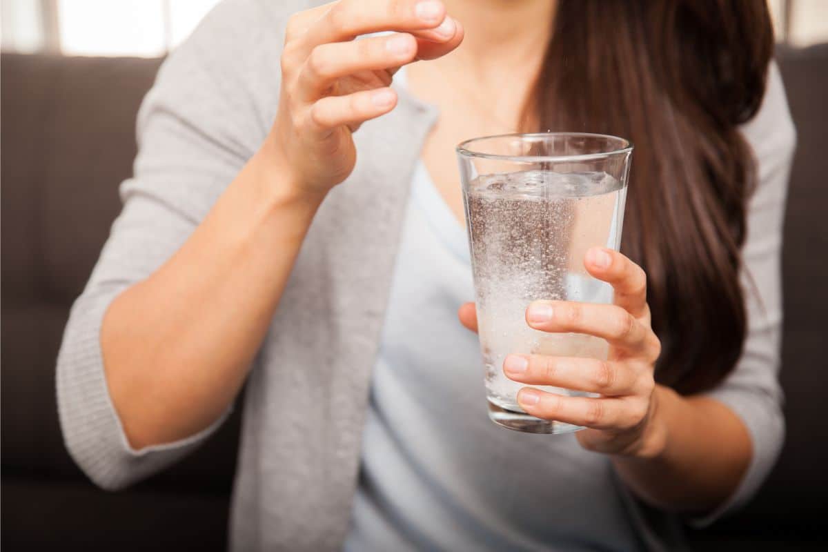 woman taking a pill with a glass of water in her hand
