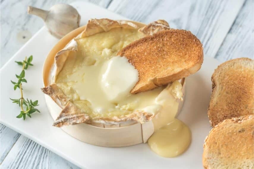 Camembert in wooden box, melted, with toasted bread slices