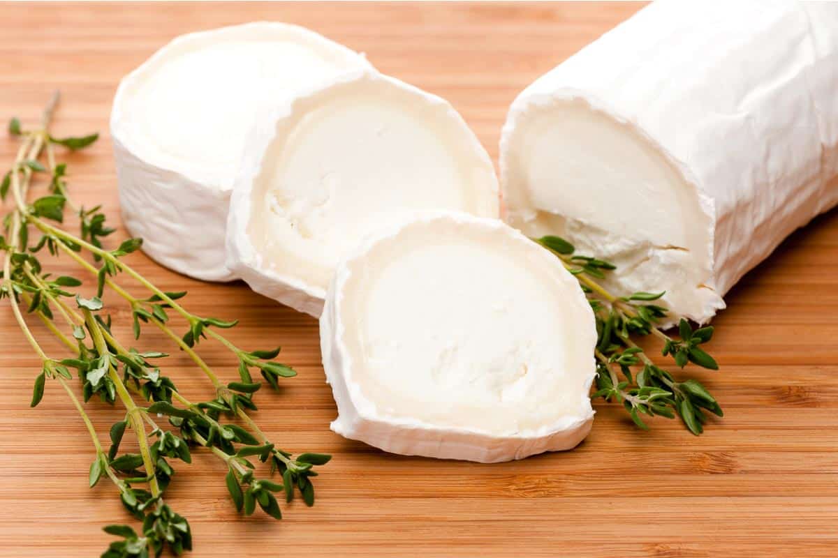 Chevre goat cheese, log, sliced, on wooden board with fresh thyme