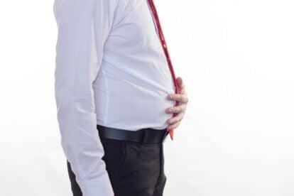 A side view of a man in a dress shirt holding his bloated belly