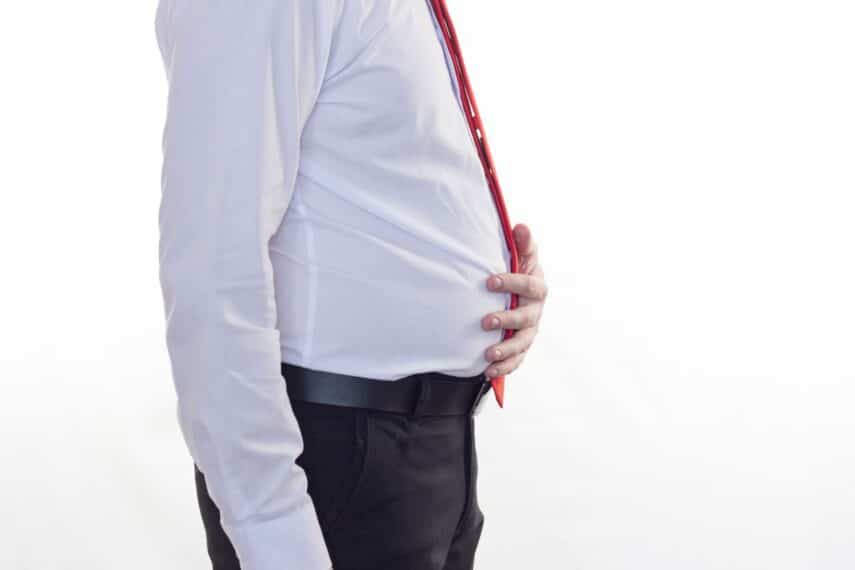 A side view of a man in a dress shirt holding his bloated belly