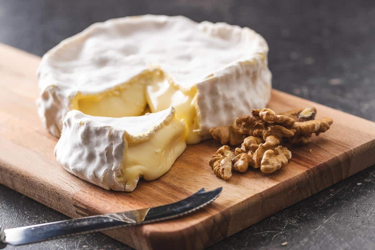 Ripe brie on a board with walnuts, wedge cut out