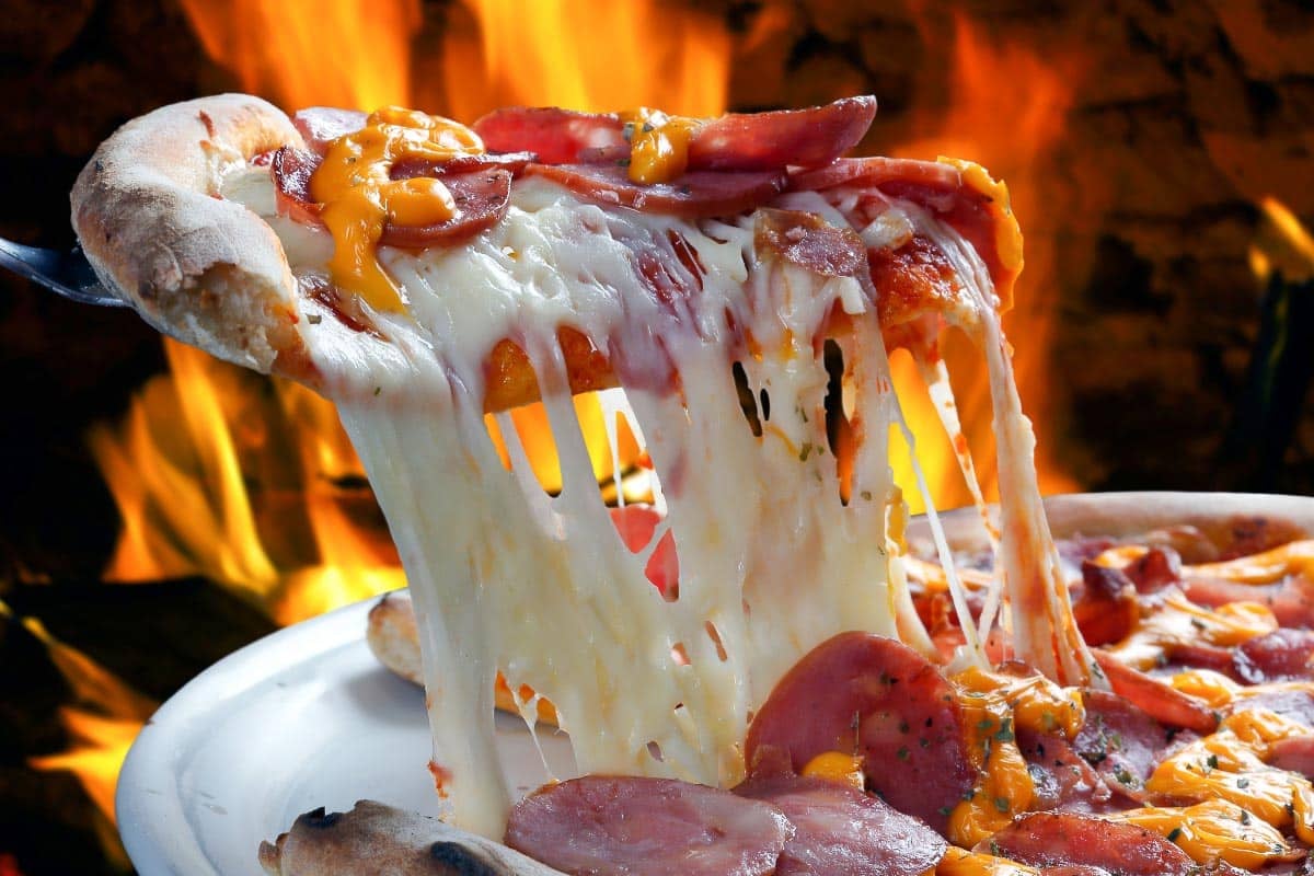 Slice of pizza being lifted from whole pizza showing melted cheese