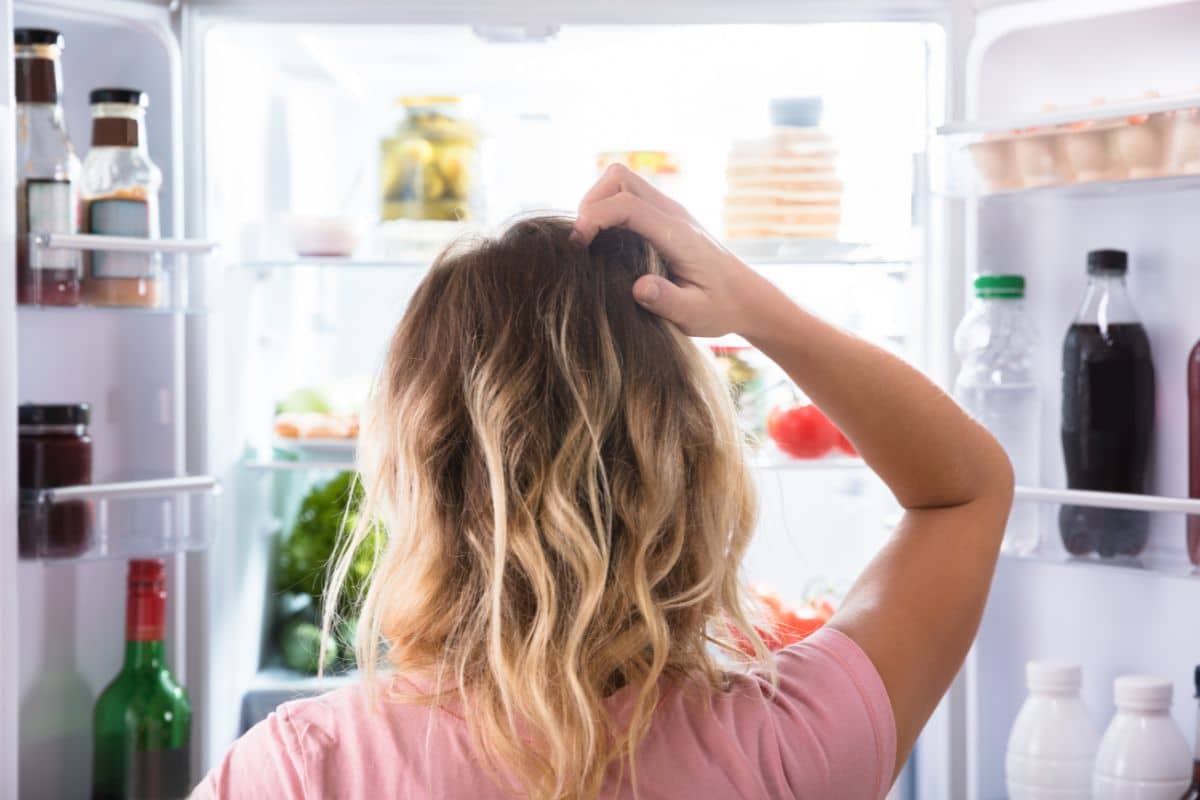Woman standing in front of open fridge wondering what to eat.