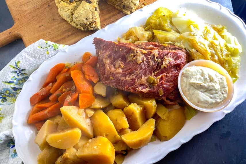 overhead image of Low FODMAP Slow Cooker Corned Beef on oval white platter with cabbage, carrots and potatoes