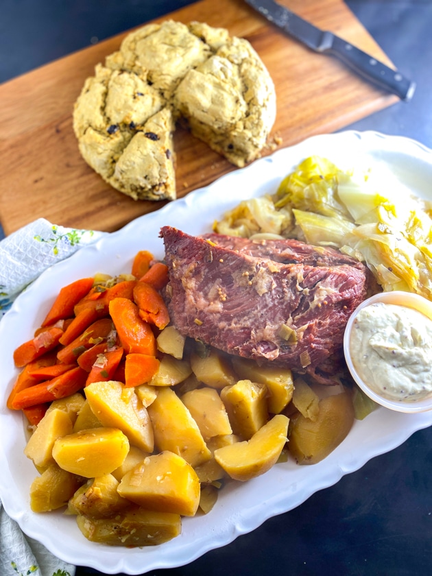 vertical image of overhead image of Low FODMAP Slow Cooker Corned Beef on oval white platter with cabbage, carrots and potatoes