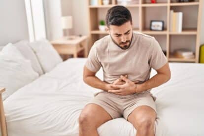 Young hispanic man suffering for stomachache sitting on bed at bedroom