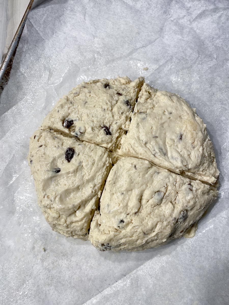Irish soda bread scored into quarters on parchment lined pan