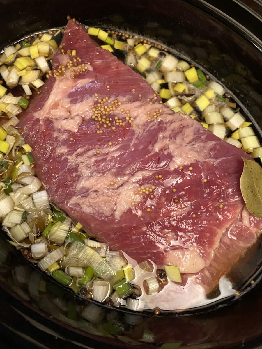 corned beef submerged in water and beer in slow cooker