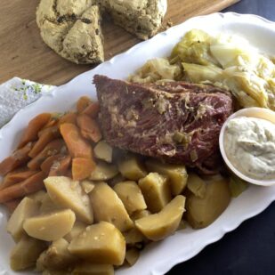 overhead image of Low FODMAP Slow Cooker Corned Beef on oval white platter with cabbage, carrots and potatoes