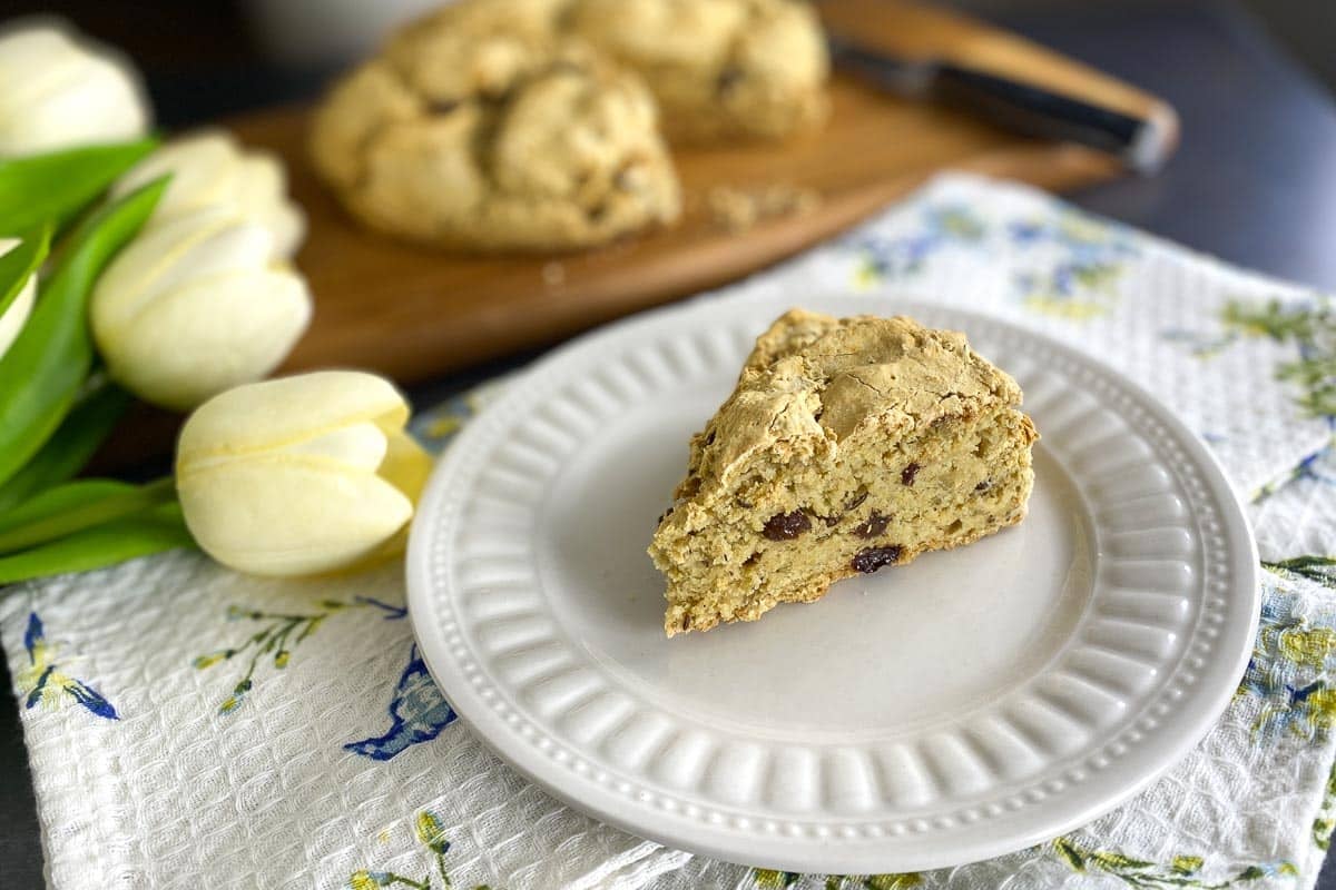 wedge of vegan low FODMAP Irish soda bread on white plate; loaf in back on wooden board