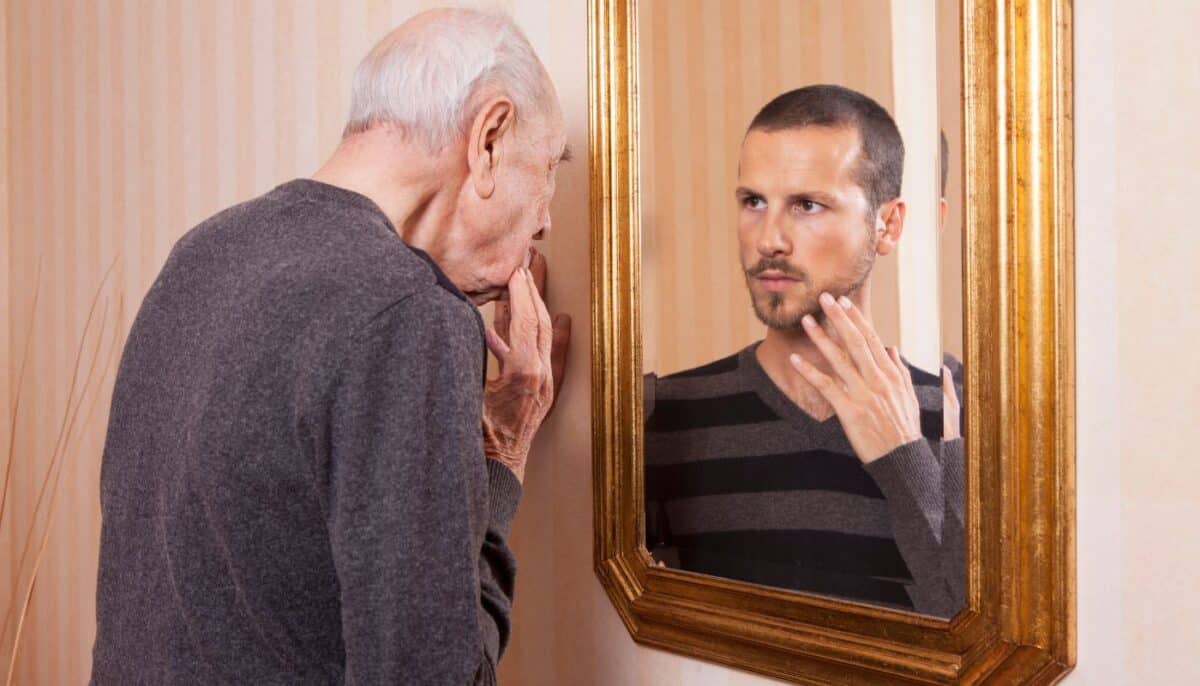 old man looking into mirror and seeing his younger self