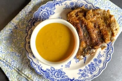 Low FODMAP Mustard BBQ Sauce in white bowl on blue and white plate with ribs.