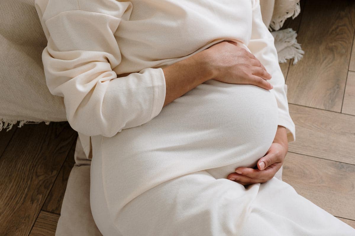 pregnant woman in white holding belly.