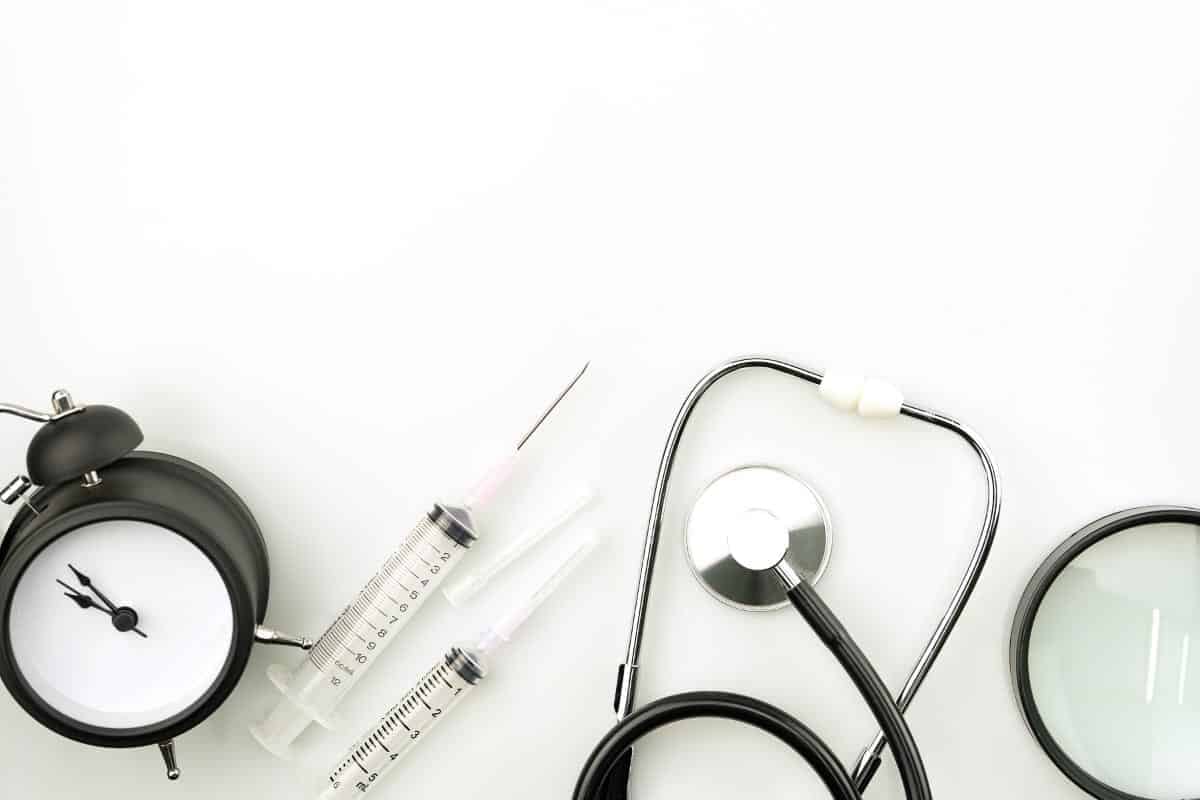 white background with clock, stethoscope and syringes.