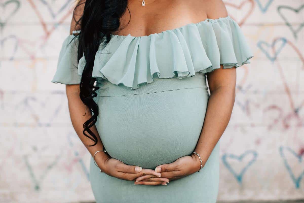 woman in pale green dress holding pregnant belly.