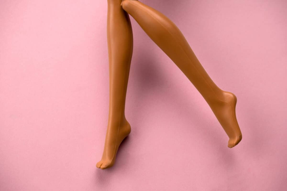 close up of smooth legs of a plastic toy doll on a soft pink background