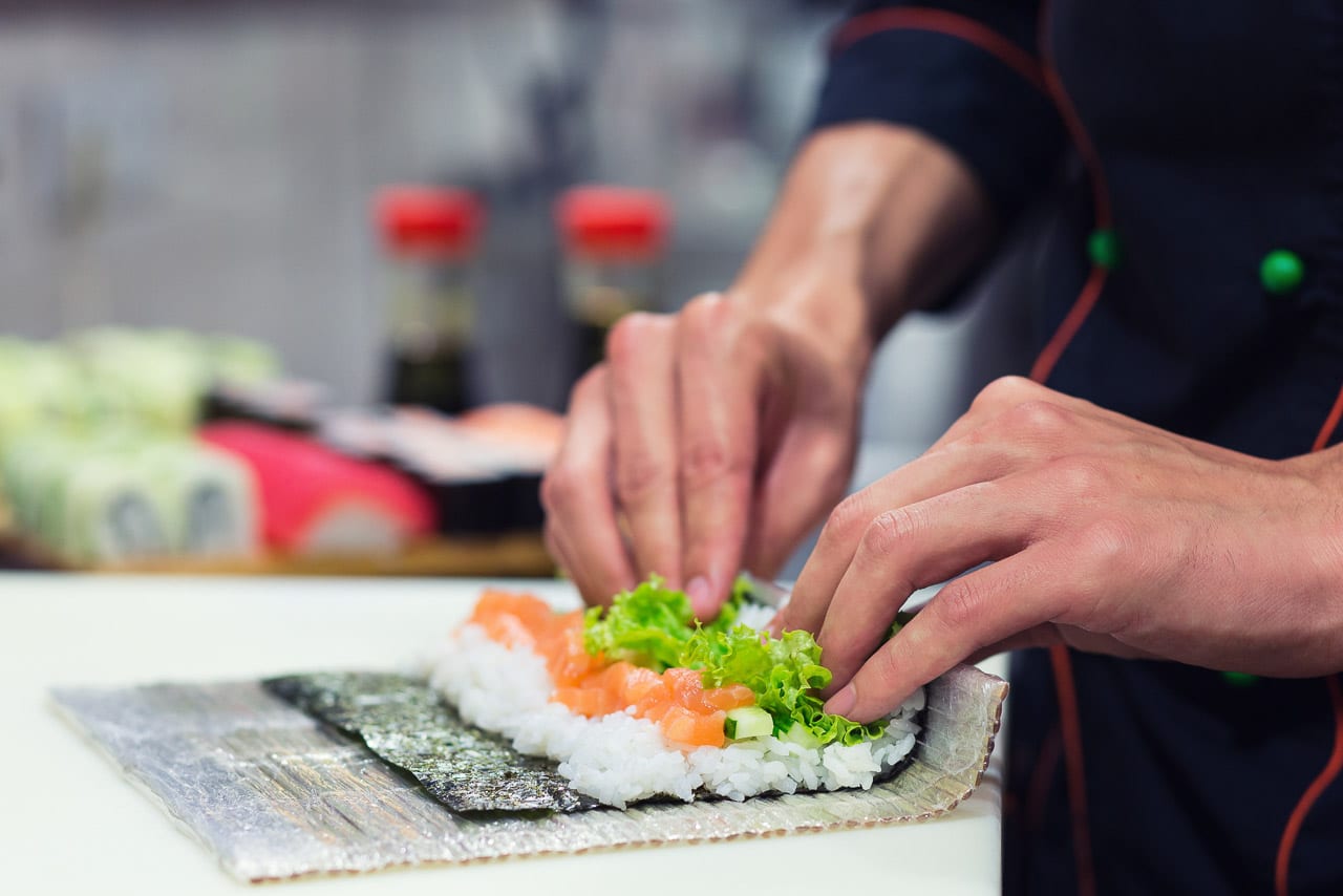 close up of hands rolling sushi using bamboo mat.