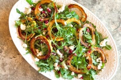 Low FODMAP Roasted Delicata Squash & Arugula Salad with Goat Cheese and Pomegranate on a white oval platter, and stone surface.