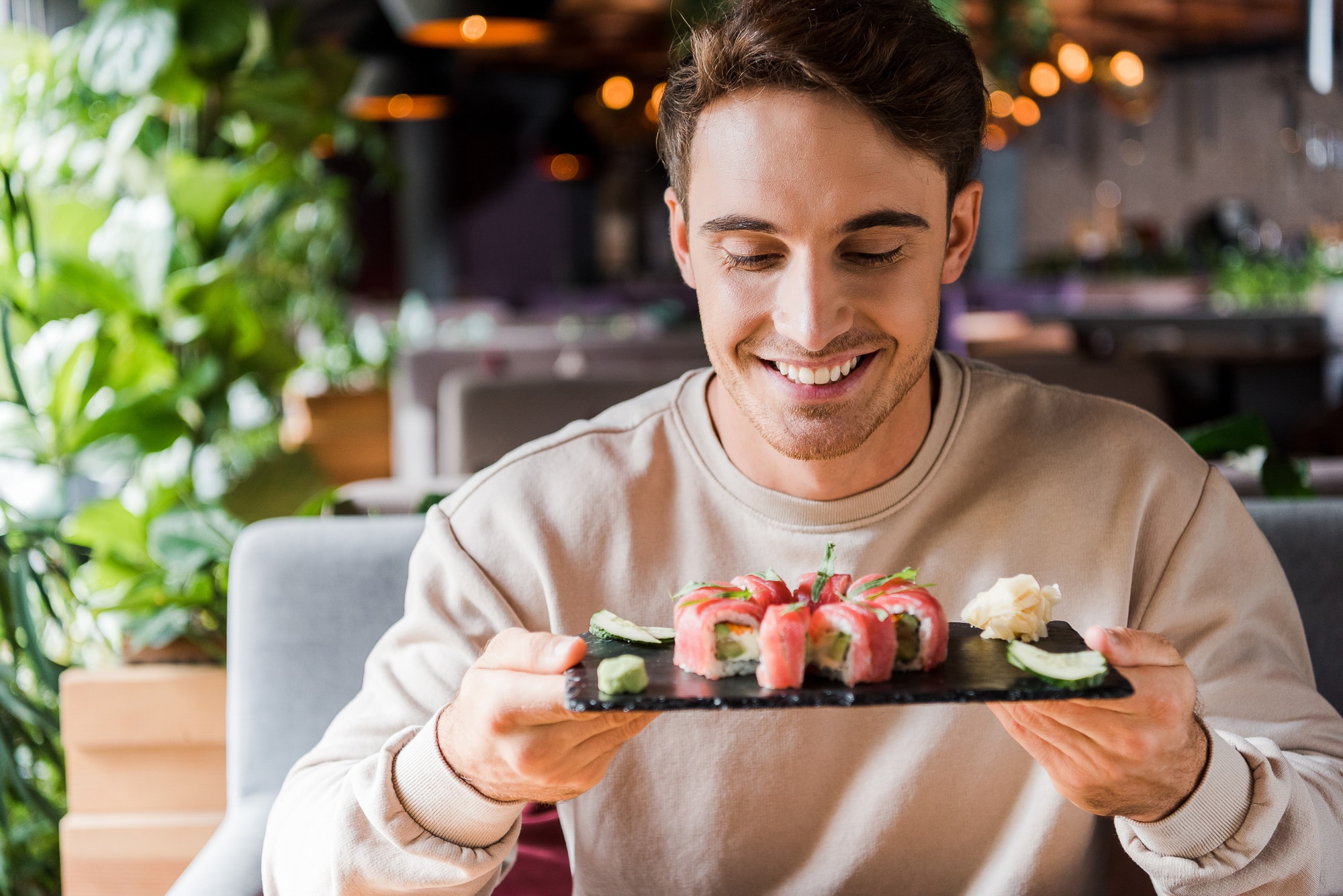 man holding sushi on dark platter.