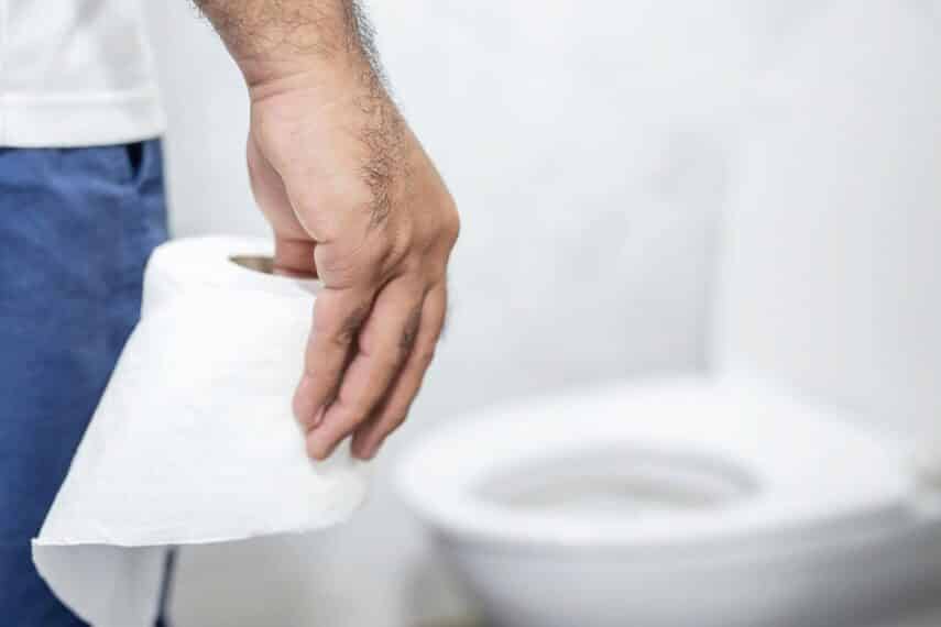man holding toilet paper looking at toilet.