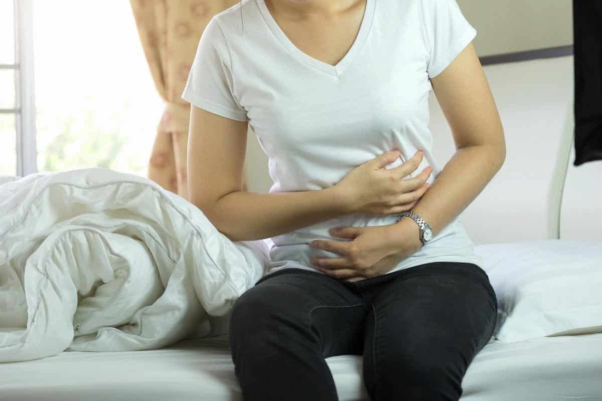 woman in white shirt holding stomach.