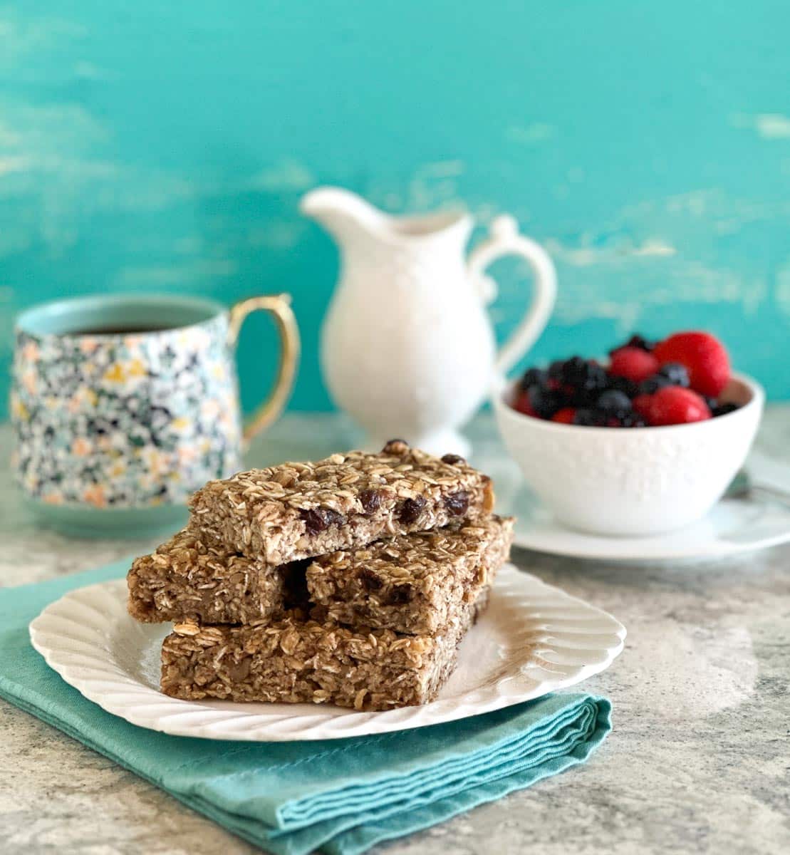Low FODMAP Breakfast Bars stacked on white plate, with aqua napkin; coffee cup in back.