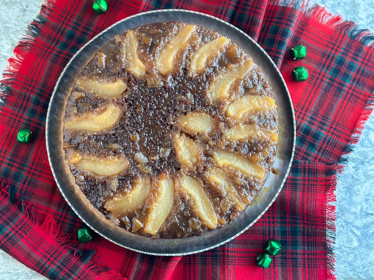 Lower FODMAP Gingerbread Pear Upside Down Cake on silver platter and red plaid napkin beneath.